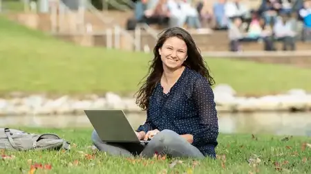 Woman sitting with laptop on grass near lake